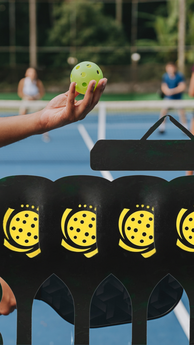 Person holding a pickleball on a court with pickleball stands in the foreground